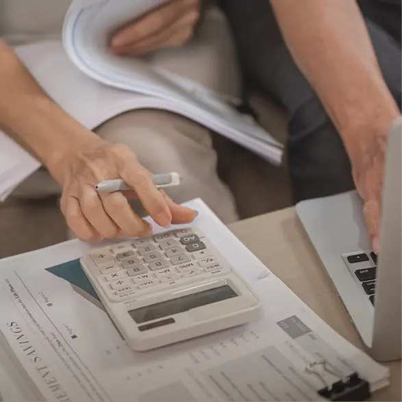 Hand nutzt Taschenrechner neben Laptop und Papieren mit Zahlen zur Kalkulation von Küchenkosten